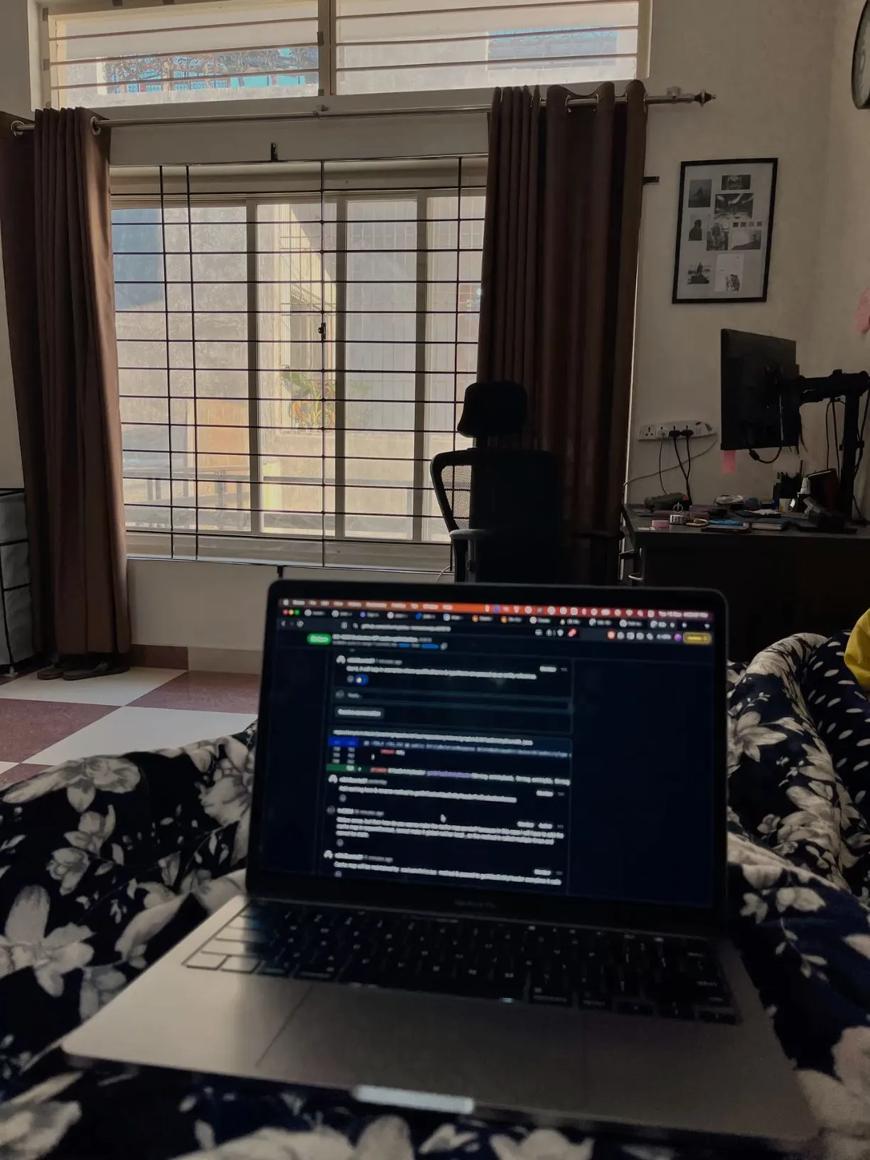 a laptop computer sitting on top of a bed in front of a window with curtains