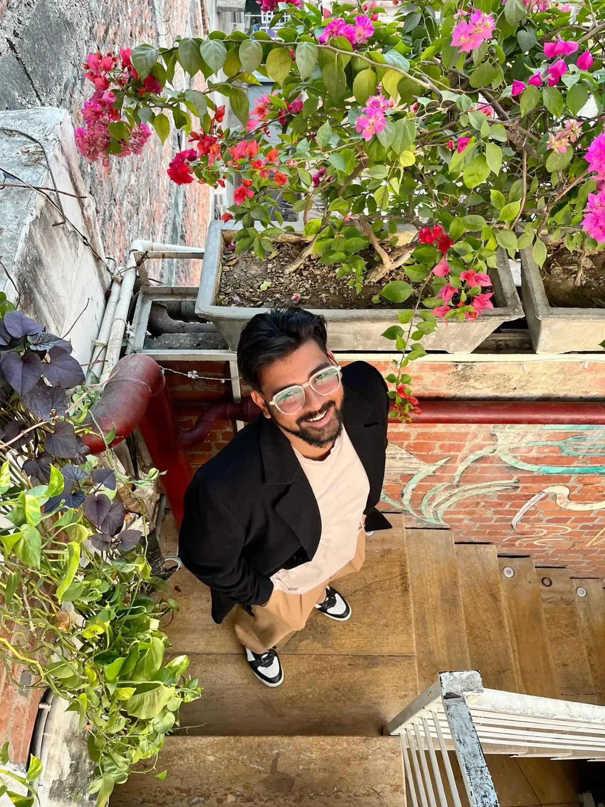 a man with glasses standing at the top of stairs looking up into the camera and smiling