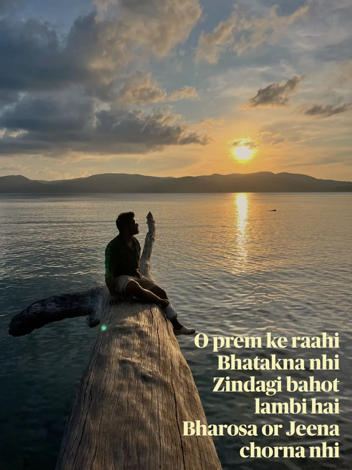 a man sitting on top of a wooden pier next to the ocean with a sunset in the background