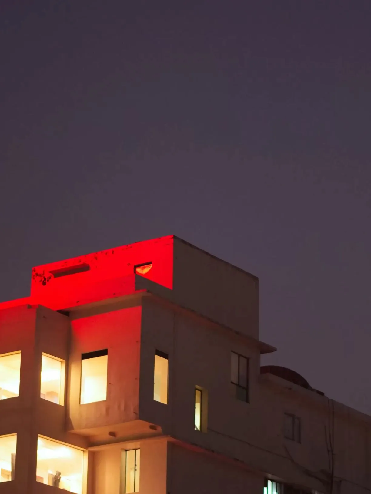 the building is lit up with red lights on it's roof and windows at night