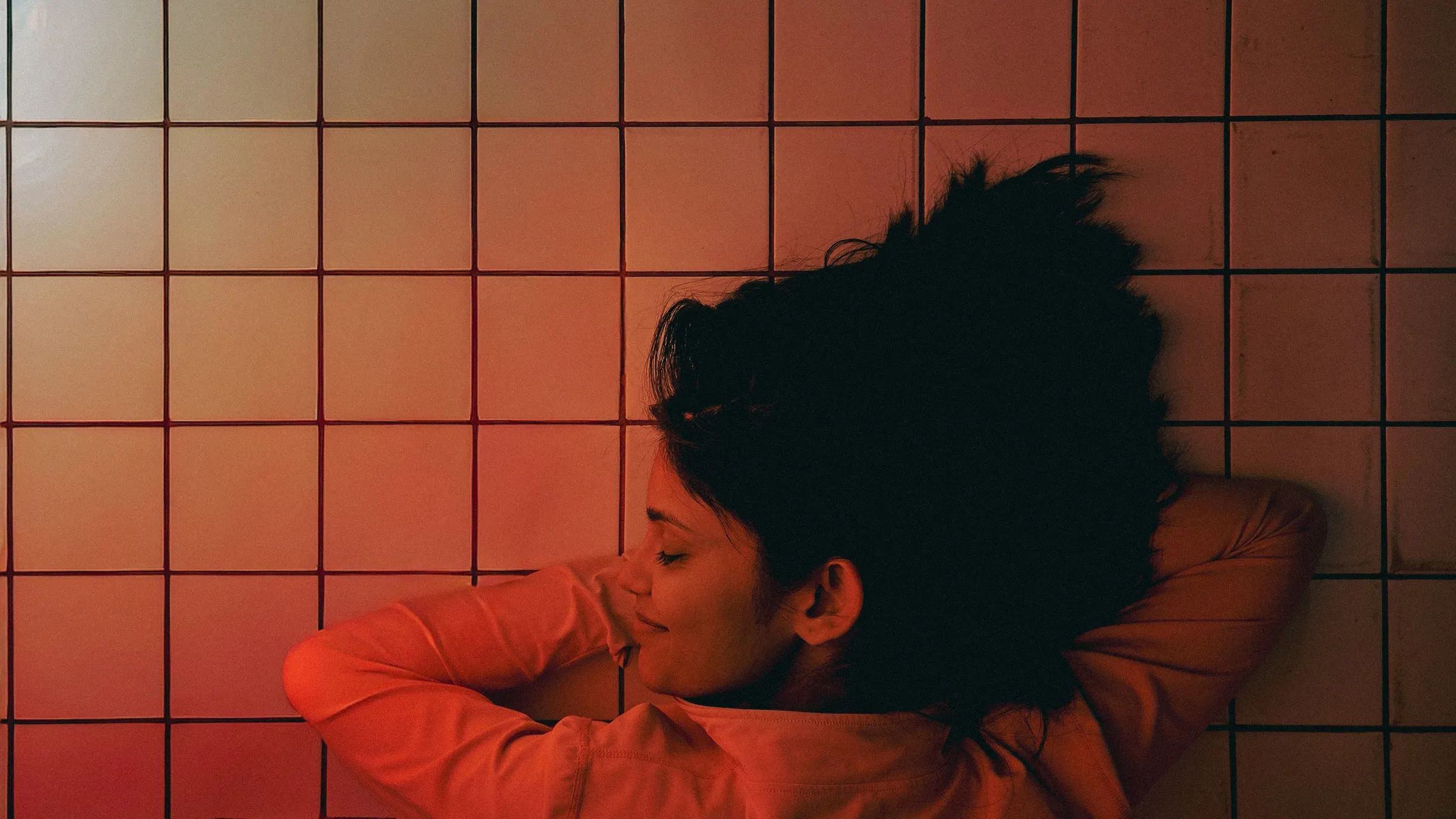 a woman laying on the floor in front of a tiled wall with her hair hanging back