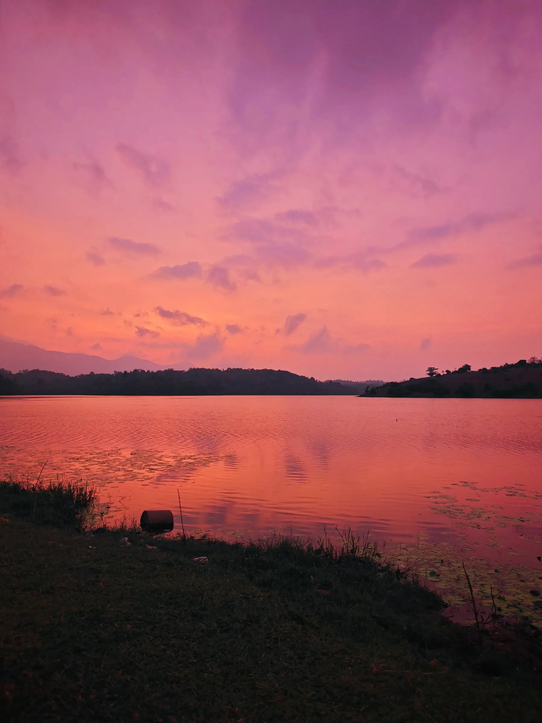 the sky is pink and purple as the sun sets over a body of water with trees in the distance