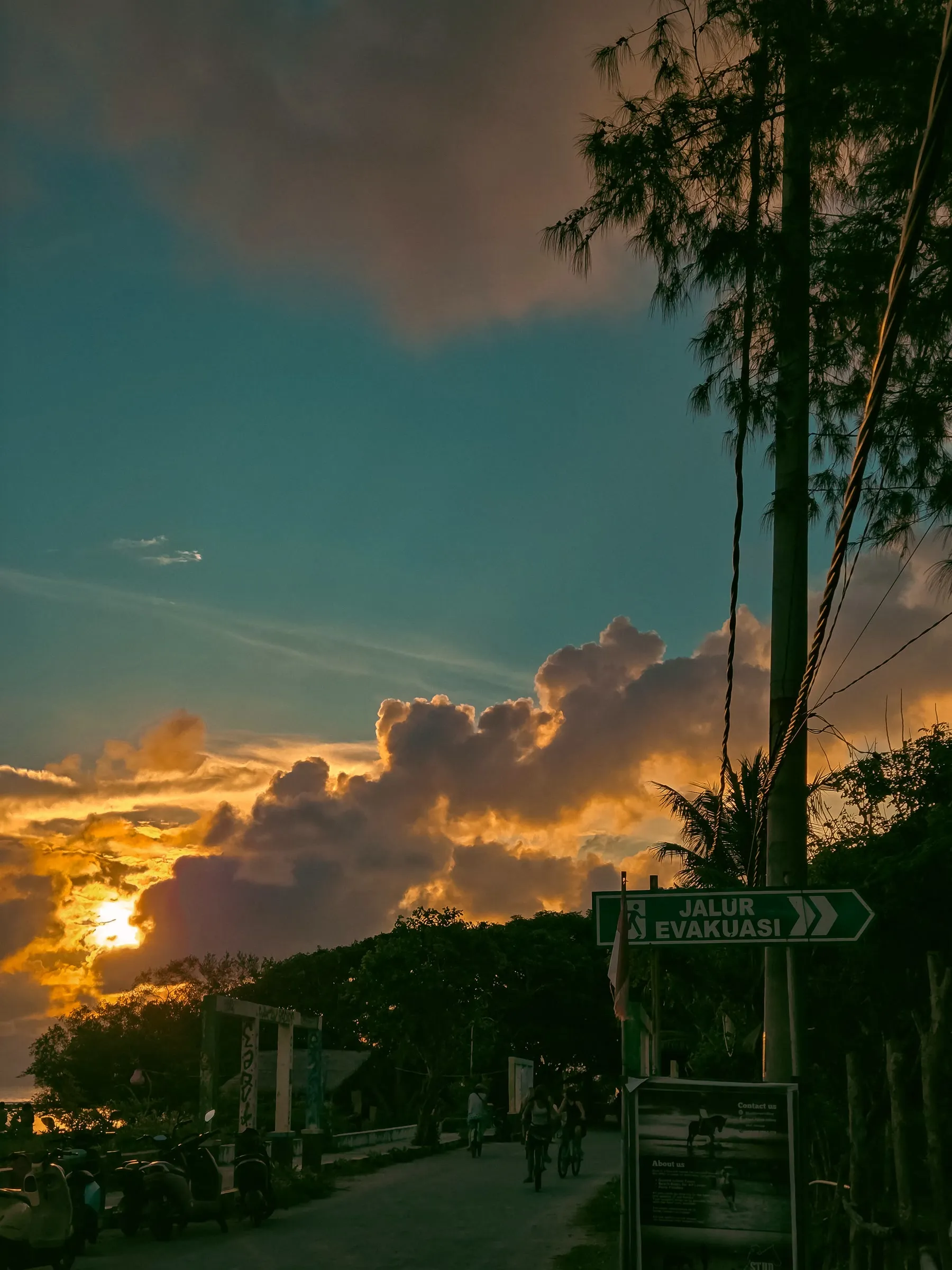 the sun is setting behind some clouds in the sky over a street with cars parked on it