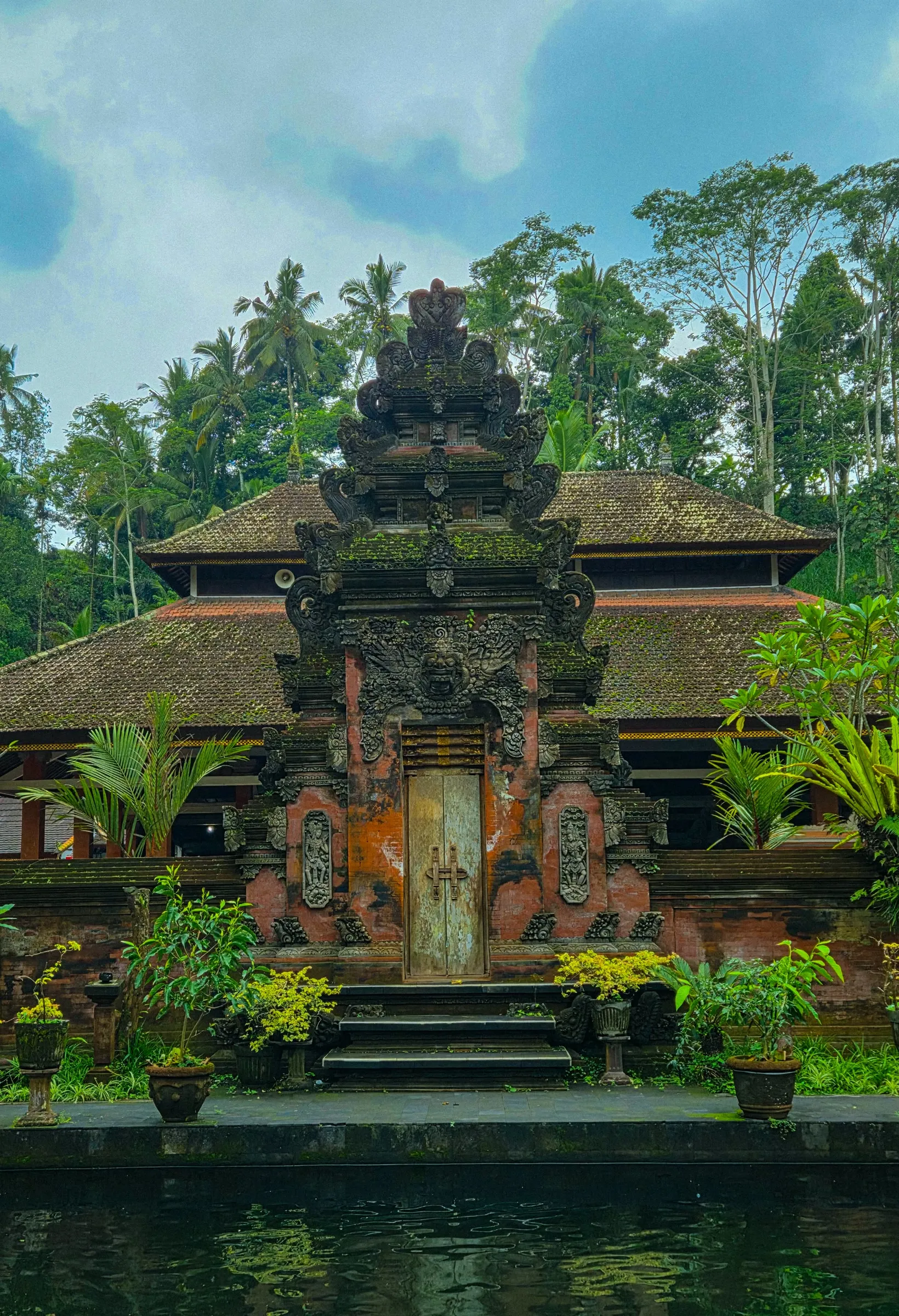 an old building sitting on top of a lake surrounded by lush green trees and plants