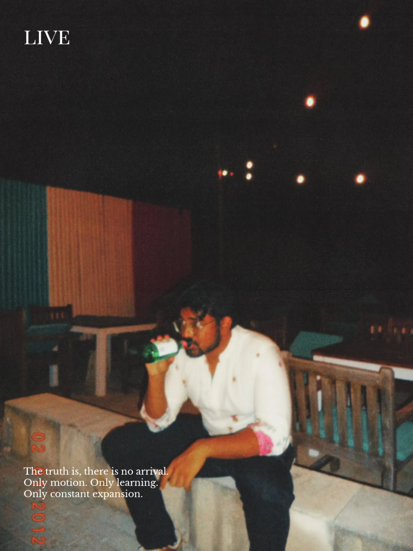 a man sitting on a bench drinking from a green bottle in front of his face