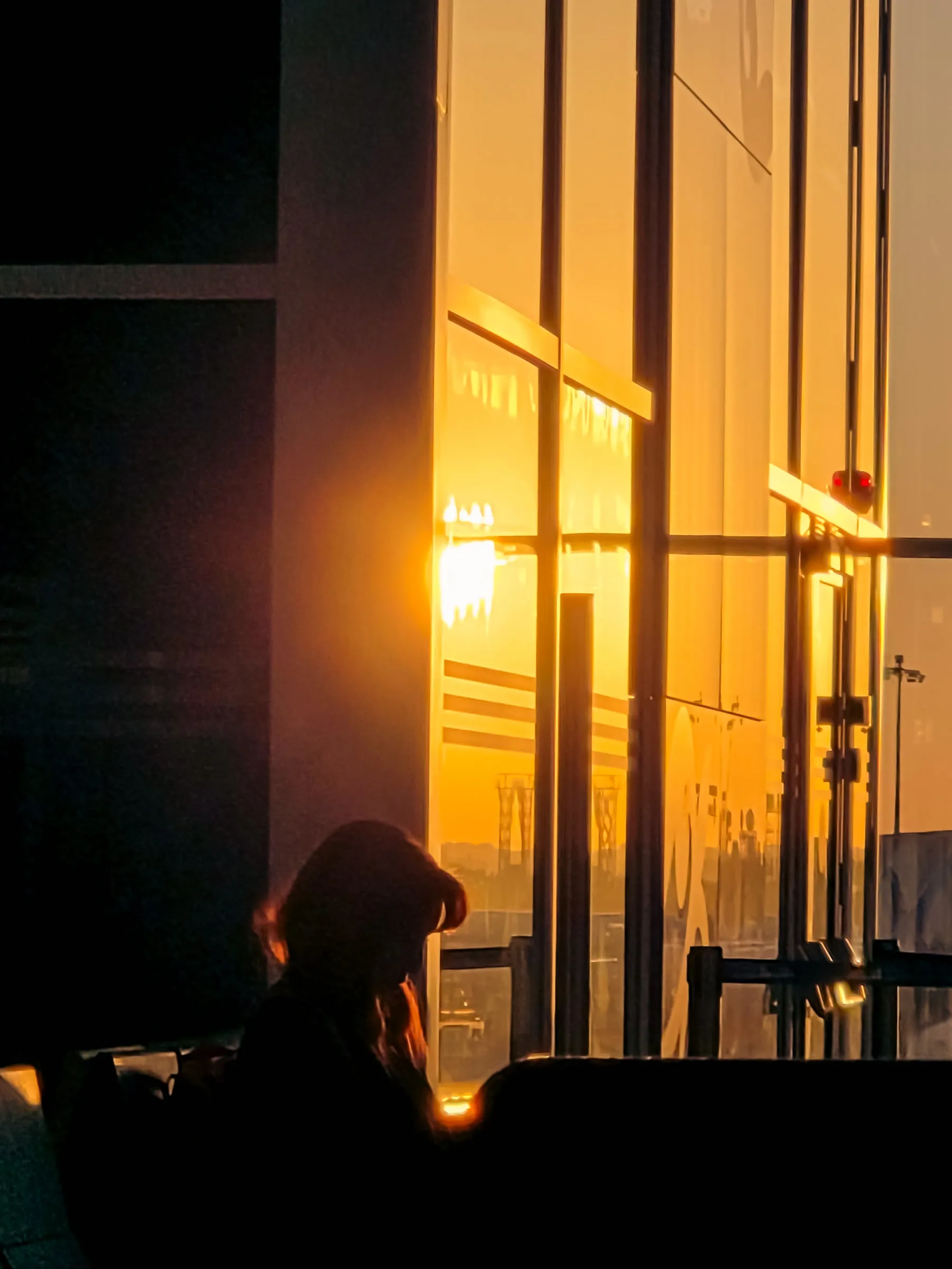 a person sitting in front of a window with the sun shining through it and buildings behind them