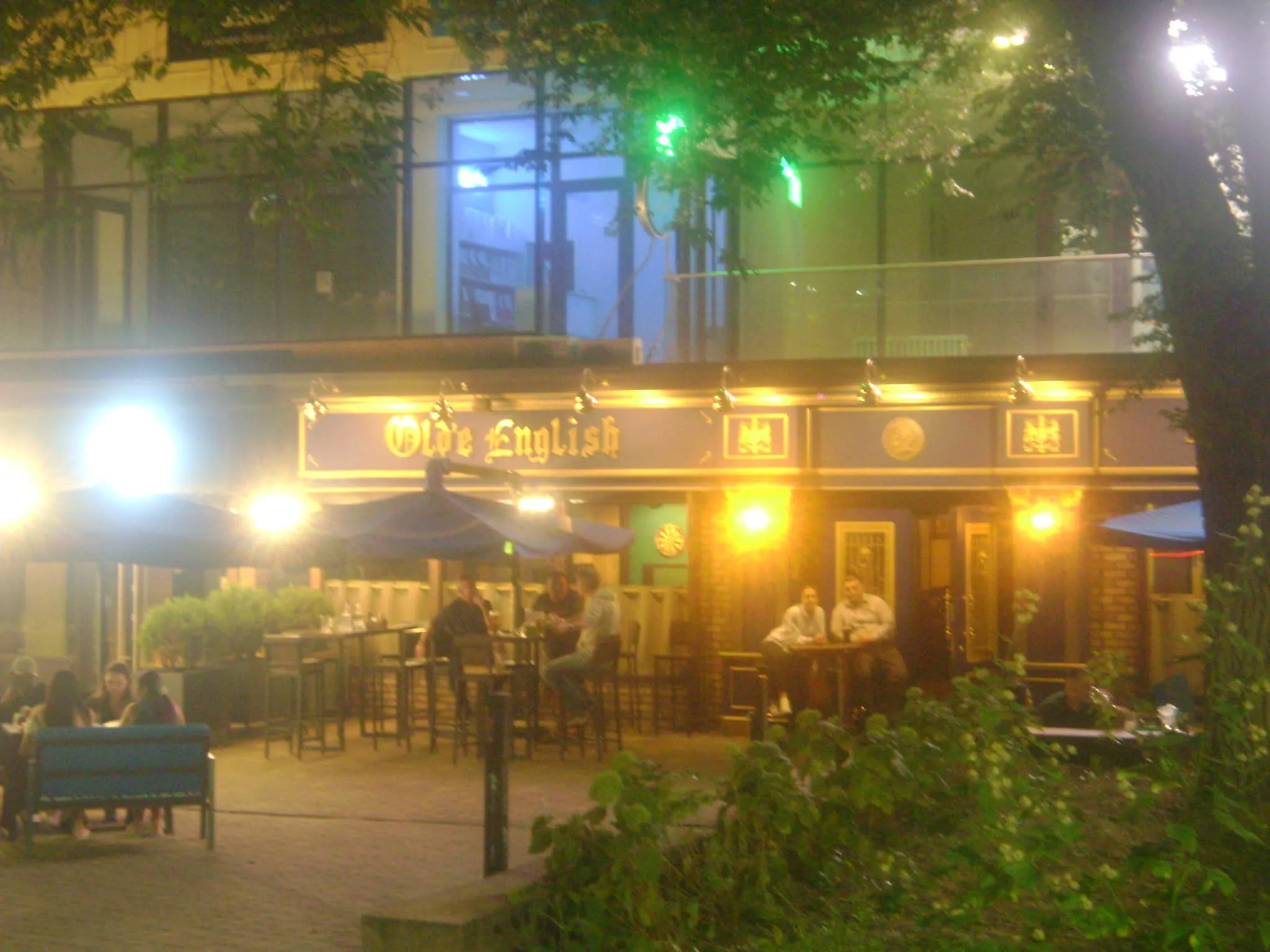 people are sitting at tables outside in front of a restaurant with lights on the windows