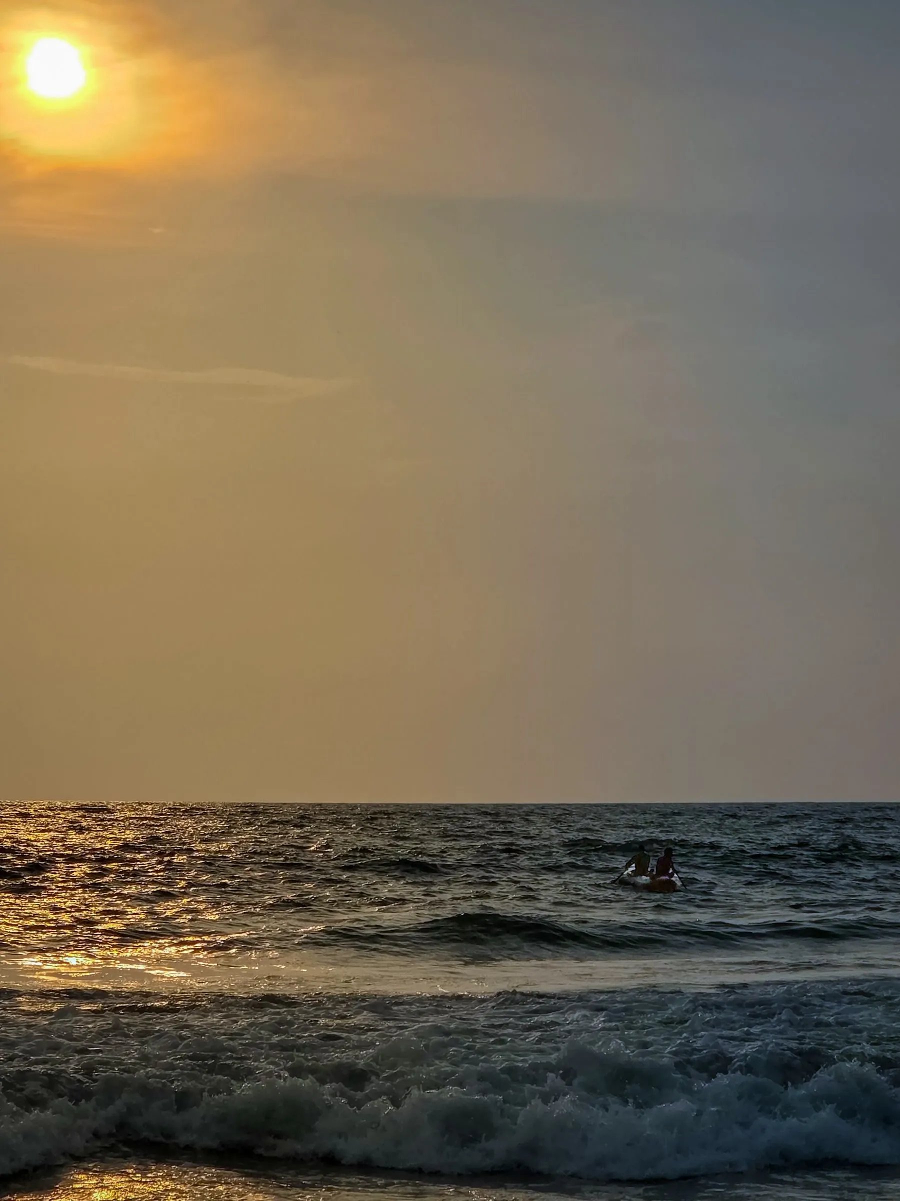 the sun is setting over the ocean with surfers out in the water on their surfboards