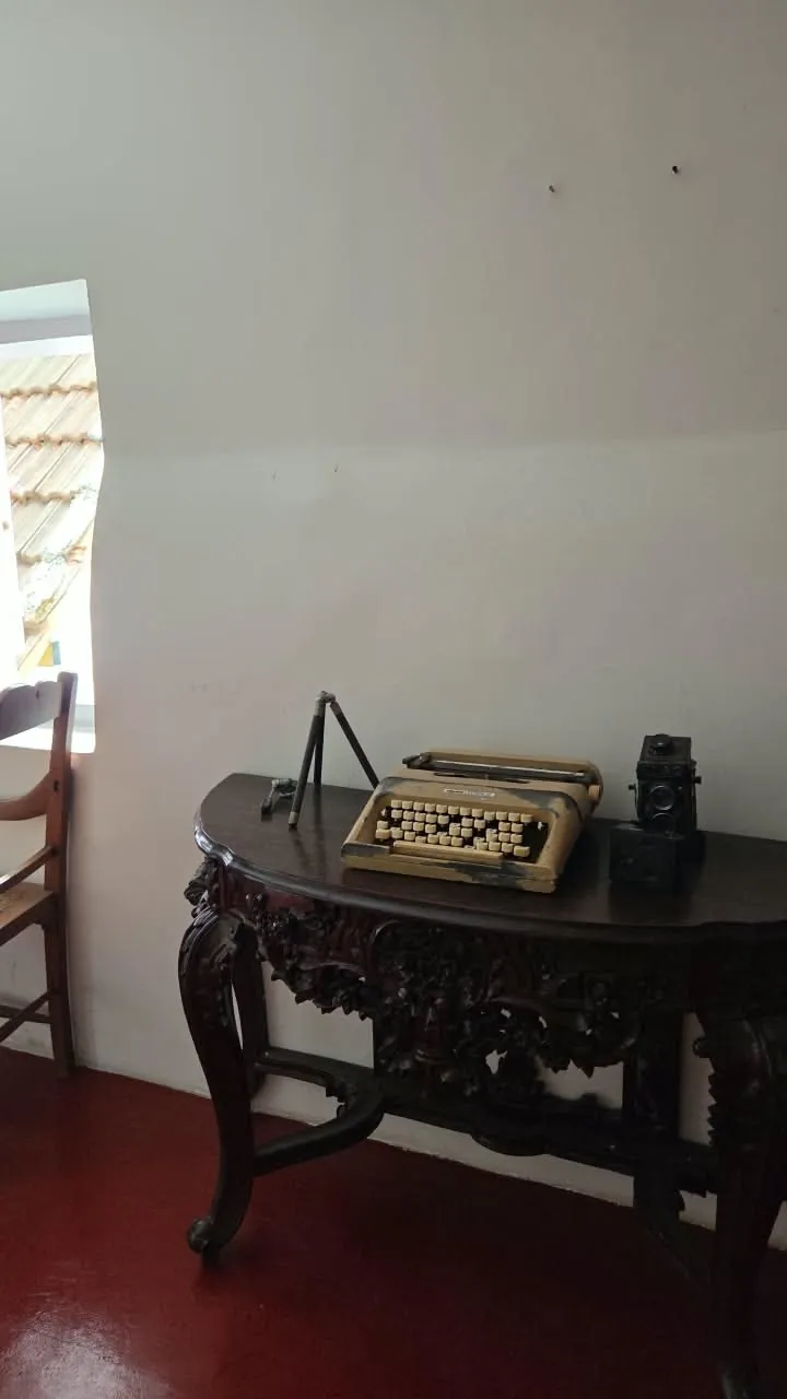an old typewriter sitting on top of a wooden table next to a chair and window