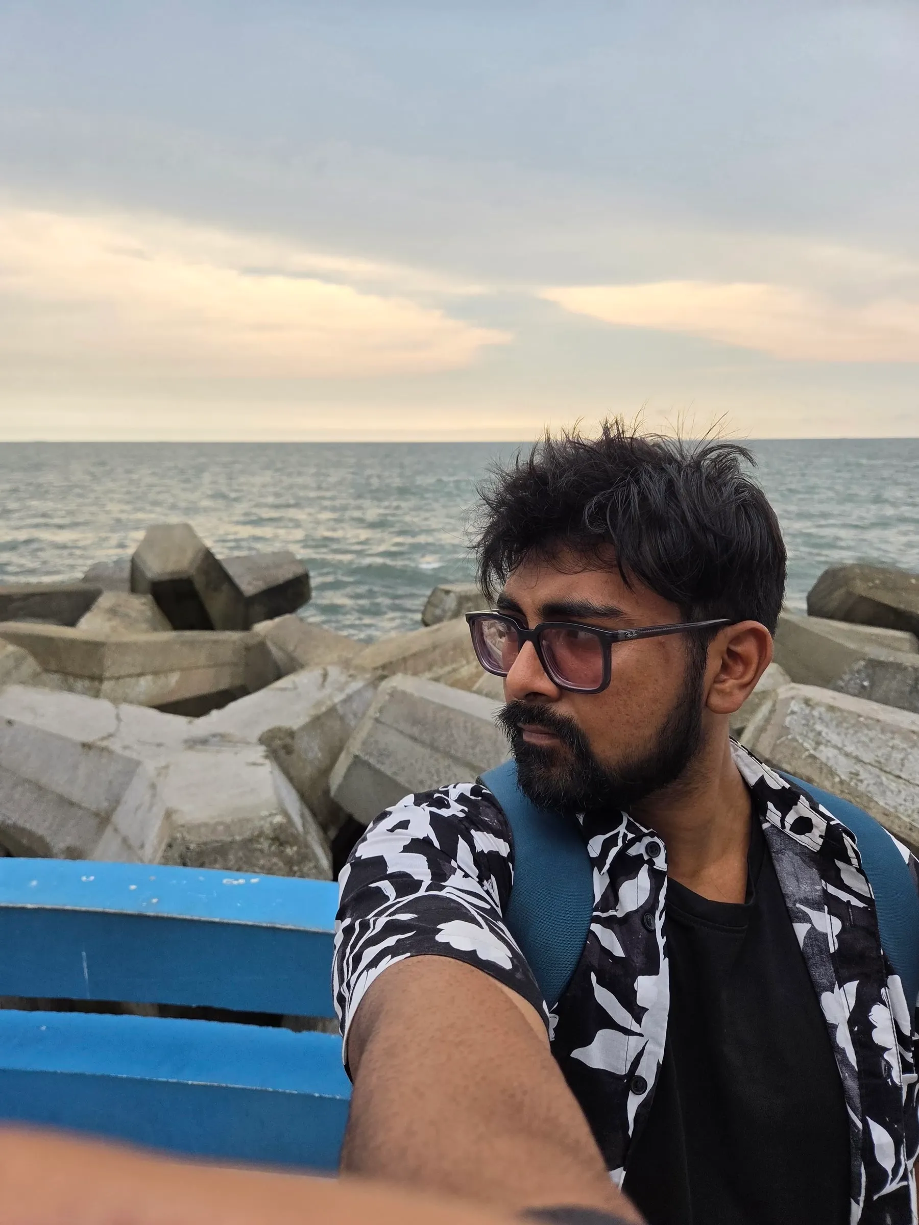 a man sitting on top of a blue bench next to the ocean in front of rocks